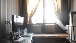 A hotel room with a desk, a computer, a window with curtains, a bed with a pillow, and a bedside table. - Chic and Cozy 2BR Apartment at Pinewood Jatinangor near JATOS (Cileunyi)