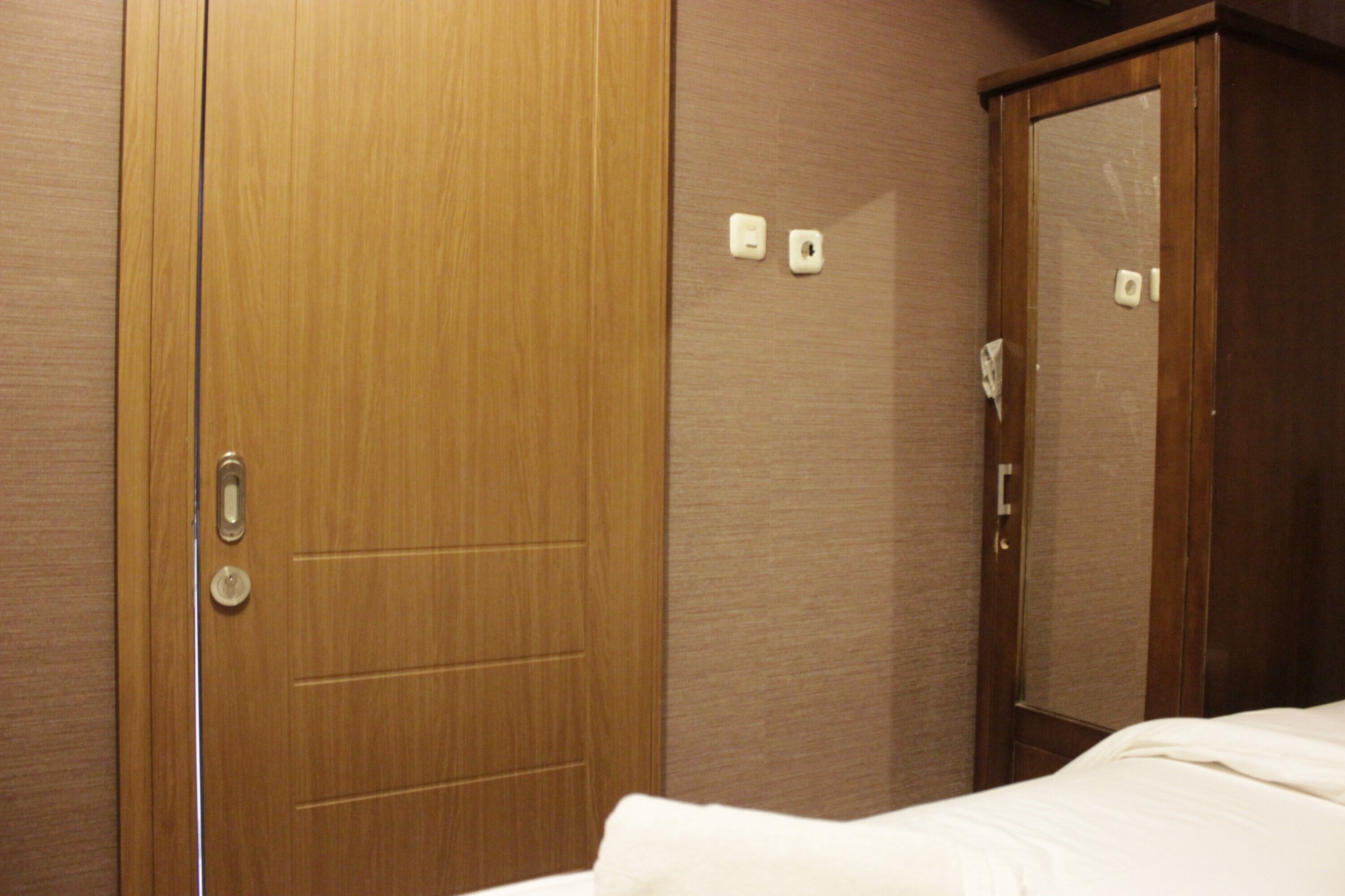A hotel room with a wooden wardrobe, a bed with white bedding, and a mirror.