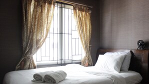 A neatly made bed with white linens and rolled towels, a window with patterned curtains, and a dark wooden headboard. - Chic and Cozy 2BR Apartment at Pinewood Jatinangor near JATOS (Cileunyi)