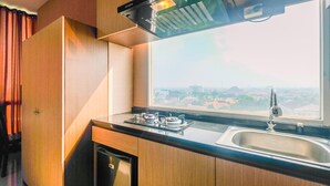 A kitchen with wooden cabinets, a gas stove, a sink, and a window overlooking a cityscape. - Compact and Simple Studio Apartment at Saladdin Mansion (Depok)