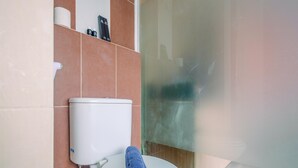 A bathroom with a toilet, a towel, and a shower area. - Compact and Simple Studio Apartment at Saladdin Mansion (Depok)