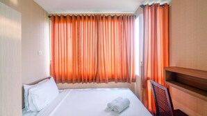 A hotel room with a bed, a chair, a wooden shelf, and orange curtains. - Compact and Simple Studio Apartment at Saladdin Mansion (Depok)