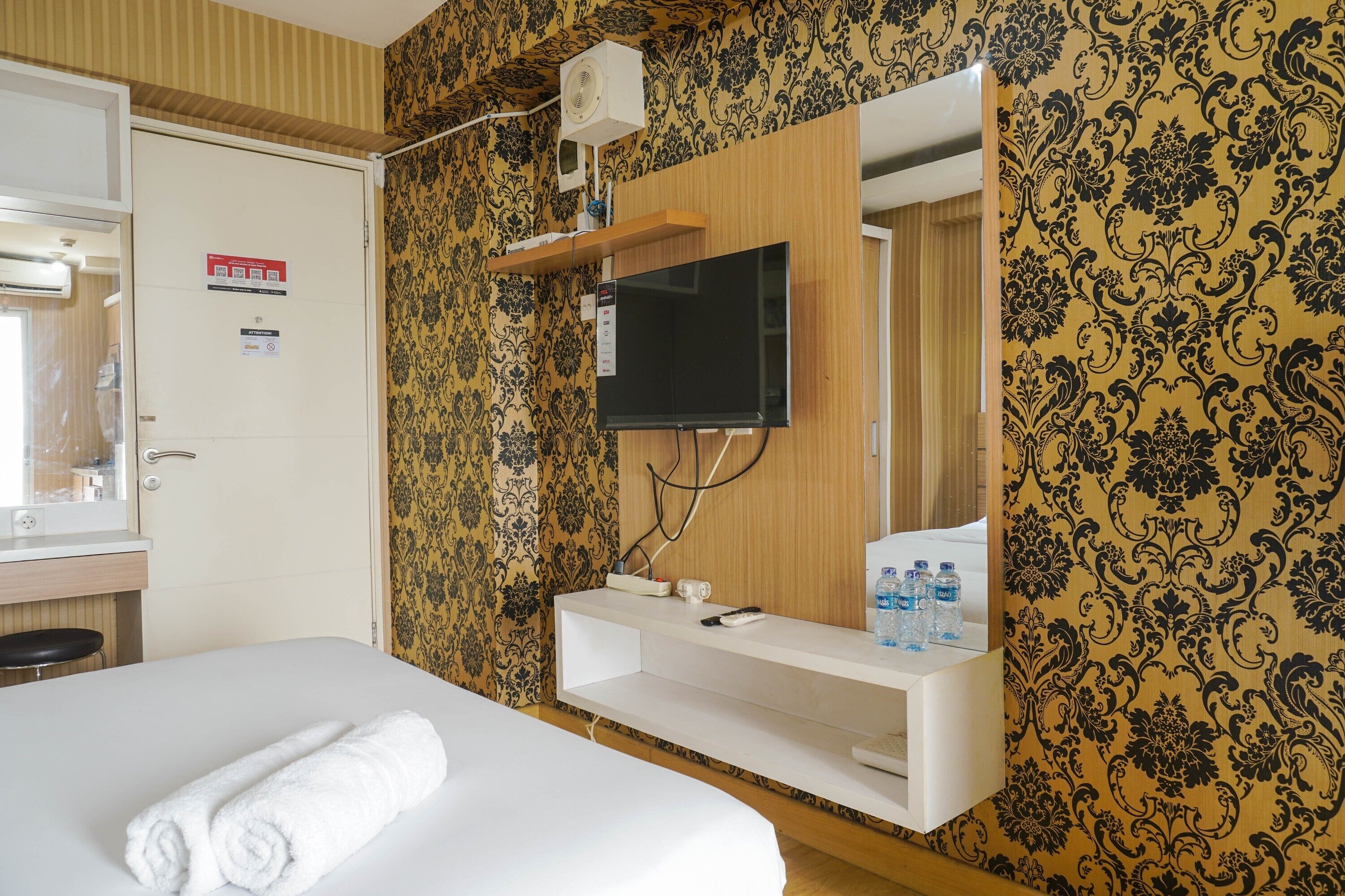 Ein Hotelzimmer mit einem Bett, einem an einer Holzplatte montierten Fernseher, einem Spiegel und einem Ablagefächer mit Pflegeprodukten.