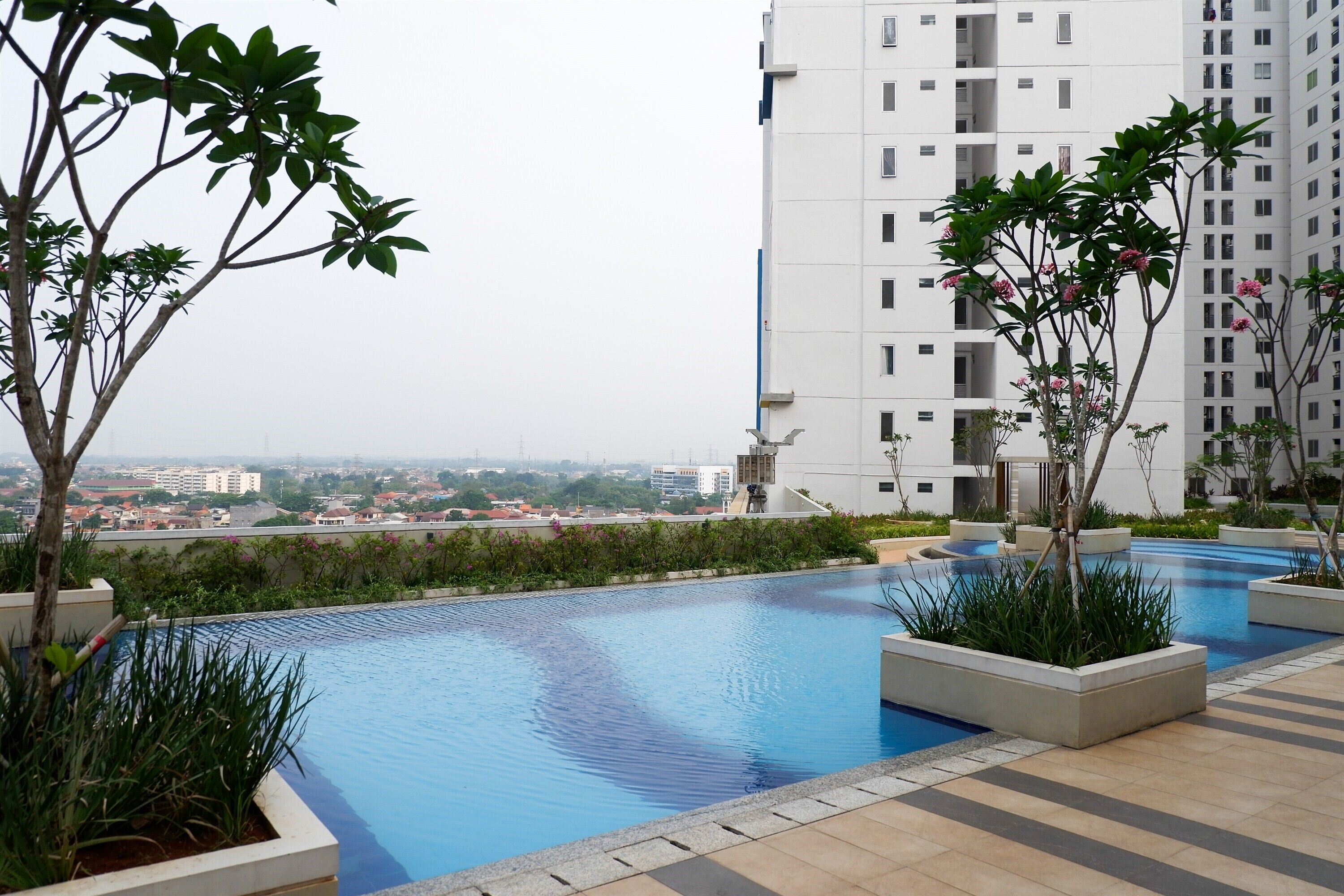 A rooftop swimming pool with a view of a cityscape, surrounded by greenery and modern buildings.
