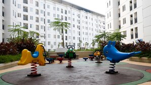 A playground with swings and a slide, surrounded by a building with multiple floors and balconies. - Good Deal Bassura City Studio Apartment near Shopping Mall (Jakarta)