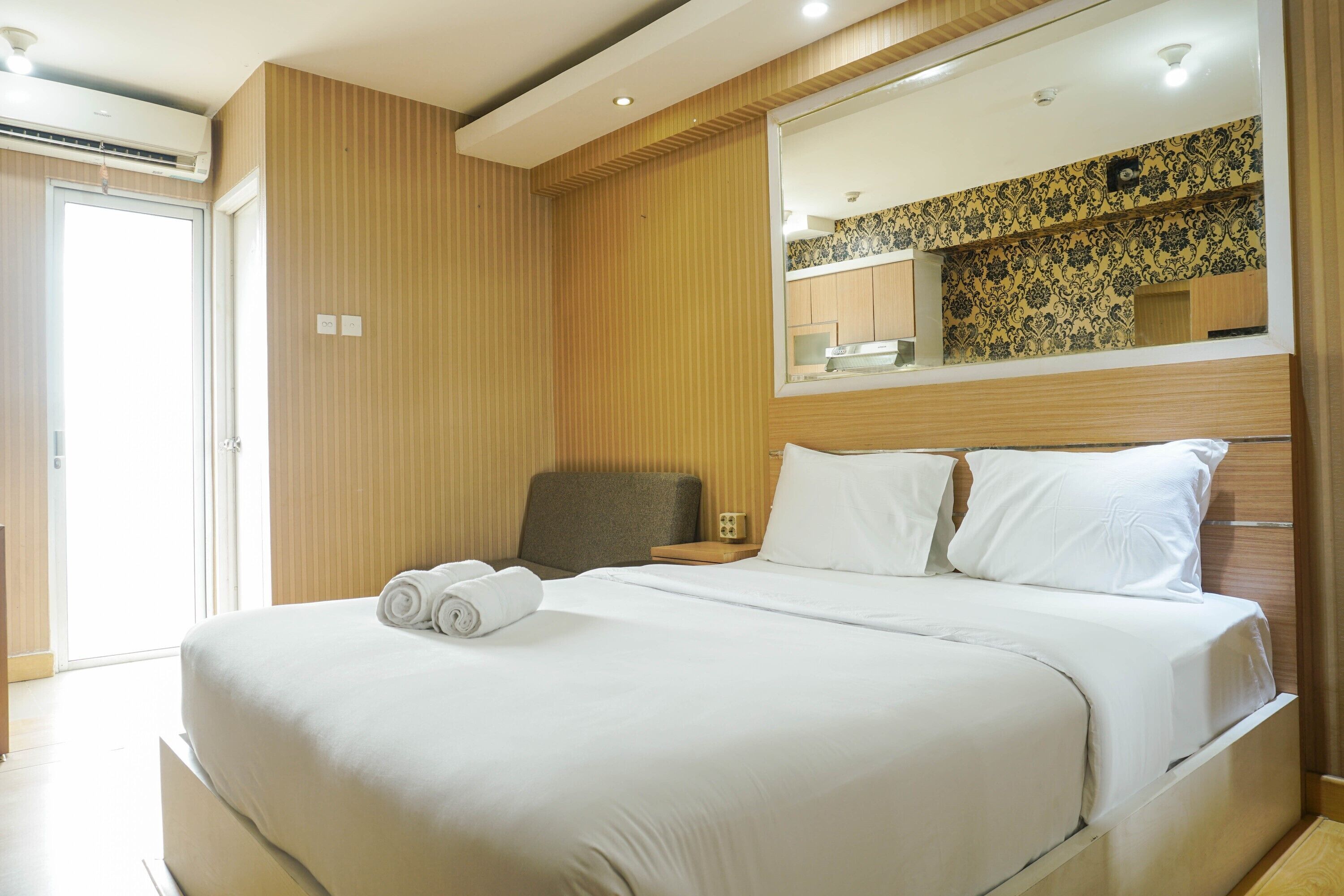 Quarto de hotel com uma cama grande, uma cadeira, uma mesa de cabeceira e um espelho.
