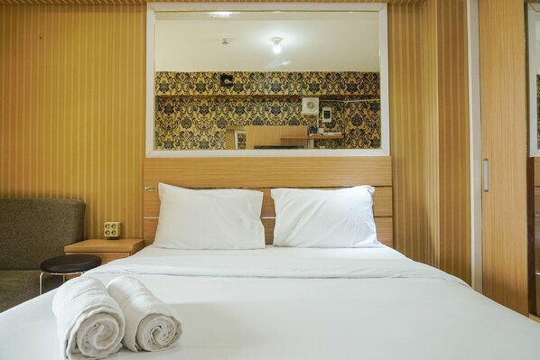 Une chambre d’hôtel avec un lit, deux oreillers, une table de chevet, une lampe et un miroir au mur.