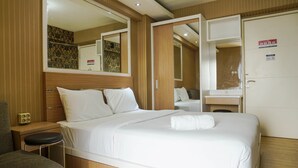 A hotel room with a large bed, a bedside table, a chair, a mirror, and a wardrobe. - Good Deal Bassura City Studio Apartment near Shopping Mall (Jakarta)