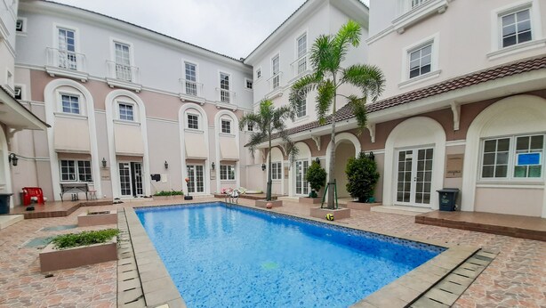 A swimming pool with a tiled deck, surrounded by a building with multiple windows and balconies.