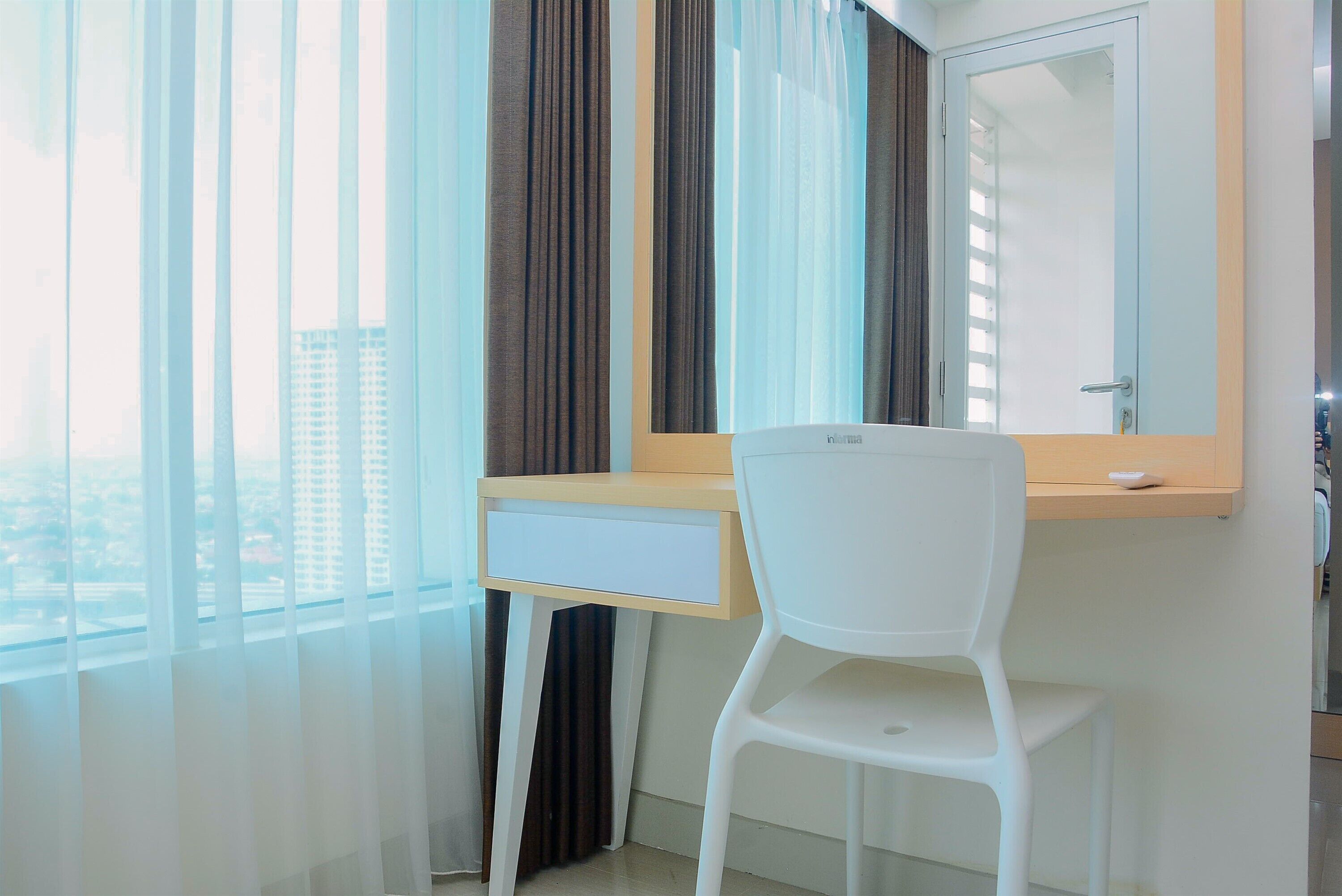 A modern room with a white desk, a chair, a large mirror, and sheer curtains.