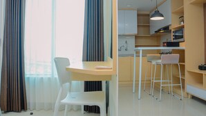 A modern kitchen with white cabinets, a bar stool, and a dining area with a table and chairs. - Grand Kamala Lagoon Studio Apartment with Modern Interior (Bekasi)
