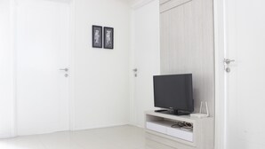 A room with a flat-screen TV on a wooden stand, white walls, and a tiled floor. - Spacious 3BR Apartment Parahyangan Residence near UNPAR (Bandung)