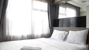 Une chambre d’hôtel avec un grand lit, du linge de lit blanc, un téléviseur à écran plat fixé au mur et des rideaux en voile.