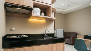 A modern kitchen with wooden cabinets, a black countertop, a stainless steel sink, and a built-in oven. - Cozy and Wonderful 1BR Ciputra International Apartment (Jakarta)