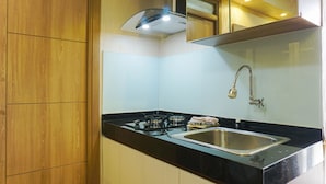 A kitchen with wooden cabinets, a black countertop, a stainless steel sink, and a gas stove. - Duri Kosambi Cozy and Relaxing 3BR Apartment at Green Palm Residence (Jakarta)