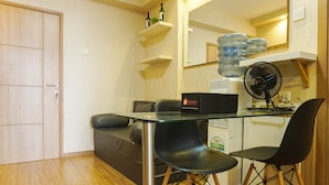 A compact living space with a glass-top dining table, two black chairs, a black sofa, a small refrigerator, and a wooden floor. - Duri Kosambi Cozy and Relaxing 3BR Apartment at Green Palm Residence (Jakarta)