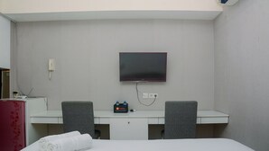 A hotel room with a bed, a desk with a flat-screen TV, two chairs, a minibar, and a telephone.