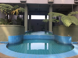 A swimming pool with blue tiles, surrounded by greenery and a building structure.