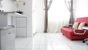 A clean, modern room with a red sofa, a small table, and a kitchenette area.