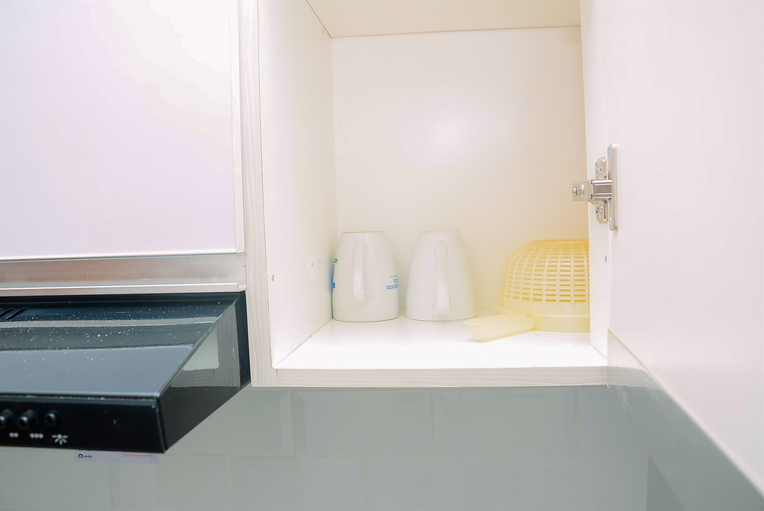Una pequeña cocina americana con un microondas, dos teteras blancas y una cesta amarilla.
