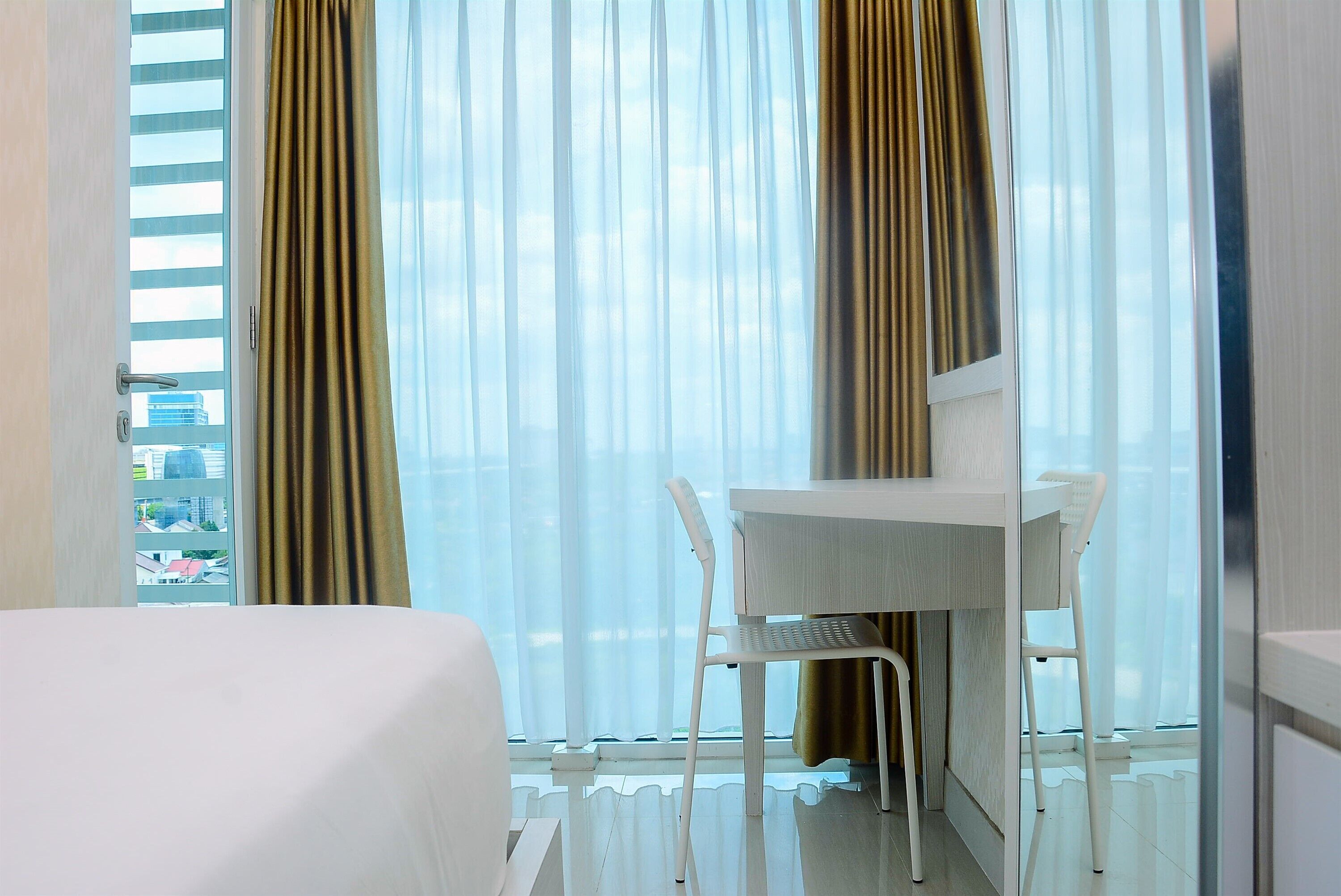 A hotel room with a bed, a desk, and a chair. There is a window with curtains.