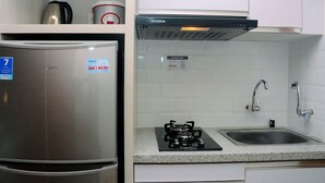 A compact kitchen with a stainless steel refrigerator, a built-in stove, a sink, and white tiled walls. - Comfy with Modern Style 1BR Grand Kamala Lagoon Apartment (Bekasi)