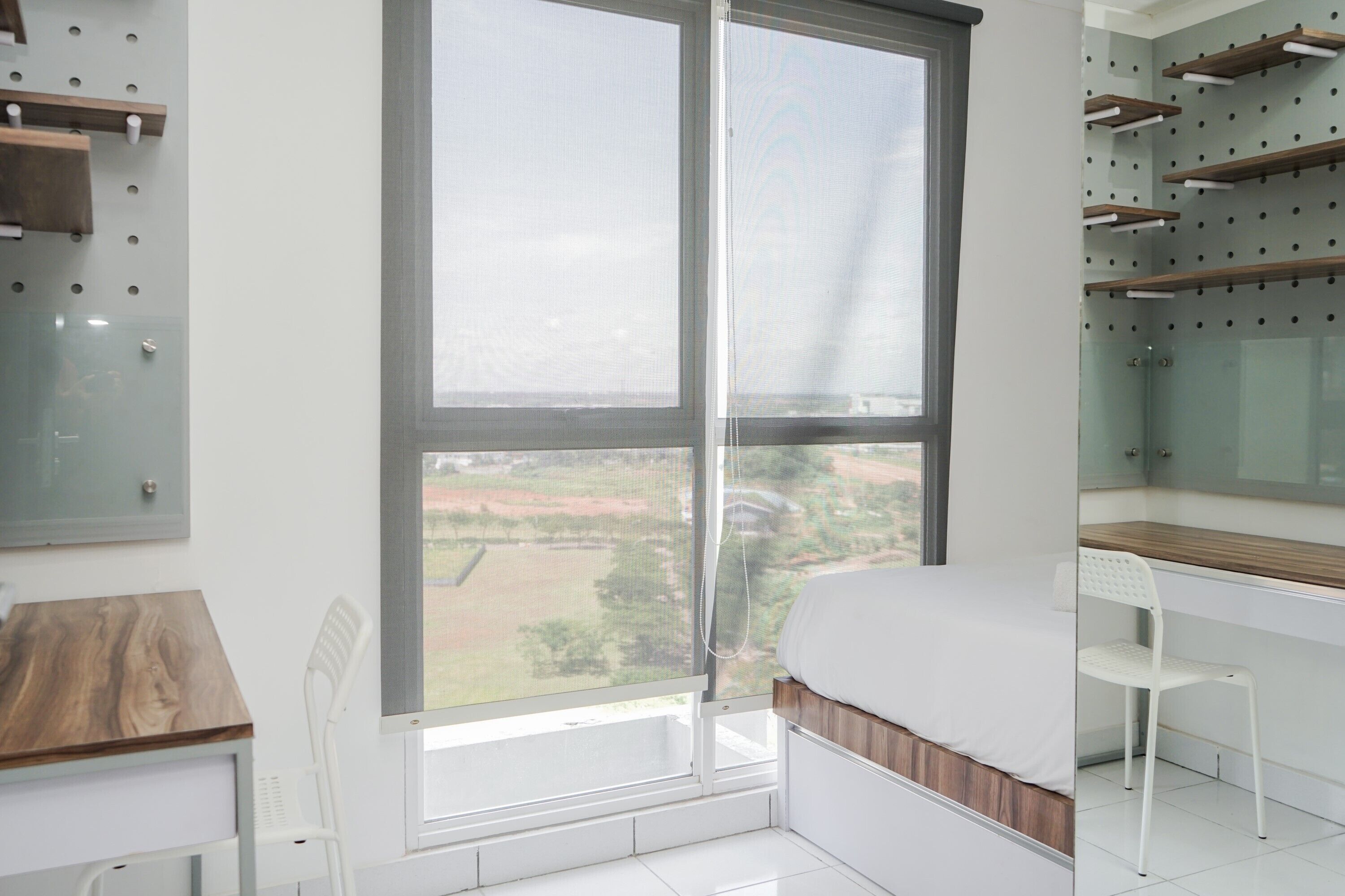 A modern bedroom with a large window, a bed, a desk, and a chair.