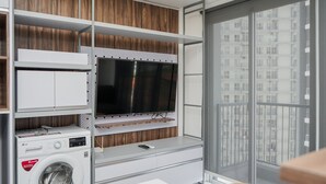 A laundry area with a washing machine, a dryer, and a television mounted on a wooden panel wall. - Premium Relaxing 2BR at Casa de Parco Apartment (South Tangerang)