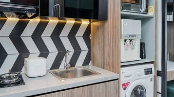 A compact kitchen with a modern design, featuring a black and white chevron backsplash, a stainless steel sink, a built-in microwave, and a front-loading washing machine.