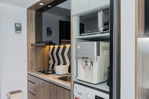 Una kitchenette compacta con microondas integrado, cafetera y un lavamanos pequeño.