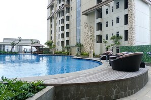 Una piscina con muelle de madera, rodeada por un edificio con balcones y un muro decorativo.