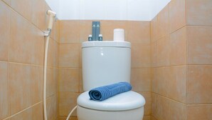Eine Toilette mit blauem Handtuch auf dem Sitz, einem Toilettenpapierhalter und einem Duschschlauch.