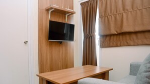 Ein Zimmer mit einem HolztV-Schrank, einem Flachbildfernseher, einem kleinen Holztisch und einem grauen Sofa.