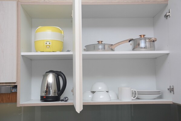 A kitchen with a microwave, kettle, pots, and white mugs on shelves.
