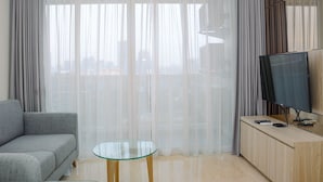 Een moderne woonkamer met een grijze bank, een glazen salontafel, een flatscreen televisie en dunne gordijnen.