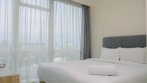 Een hotelkamer met een bed, een nachtkastje en uitzicht door dunne gordijnen.