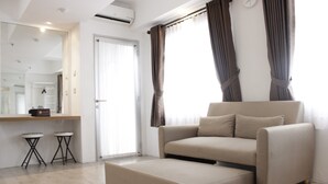 Ein modernes Wohnzimmer mit einer Couch, einem Hocker und zwei kleinen Schemeln. Im Hintergrund sind ein großer Spiegel und eine Tür zu sehen.