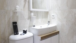 Ein modernes Badezimmer mit einem weißen Waschbecken, Spiegel und Pflegeprodukten auf einem weißen Fußboden.