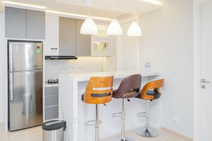 Una cocina moderna con un refrigerador de acero inoxidable, horno empotrado y encimera de mármol. Hay tres taburetes de bar de madera con patas de metal.