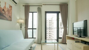 Habitación de hotel con cama, una mesita de vidrio, televisor y vistas a edificios a través de las ventanas.