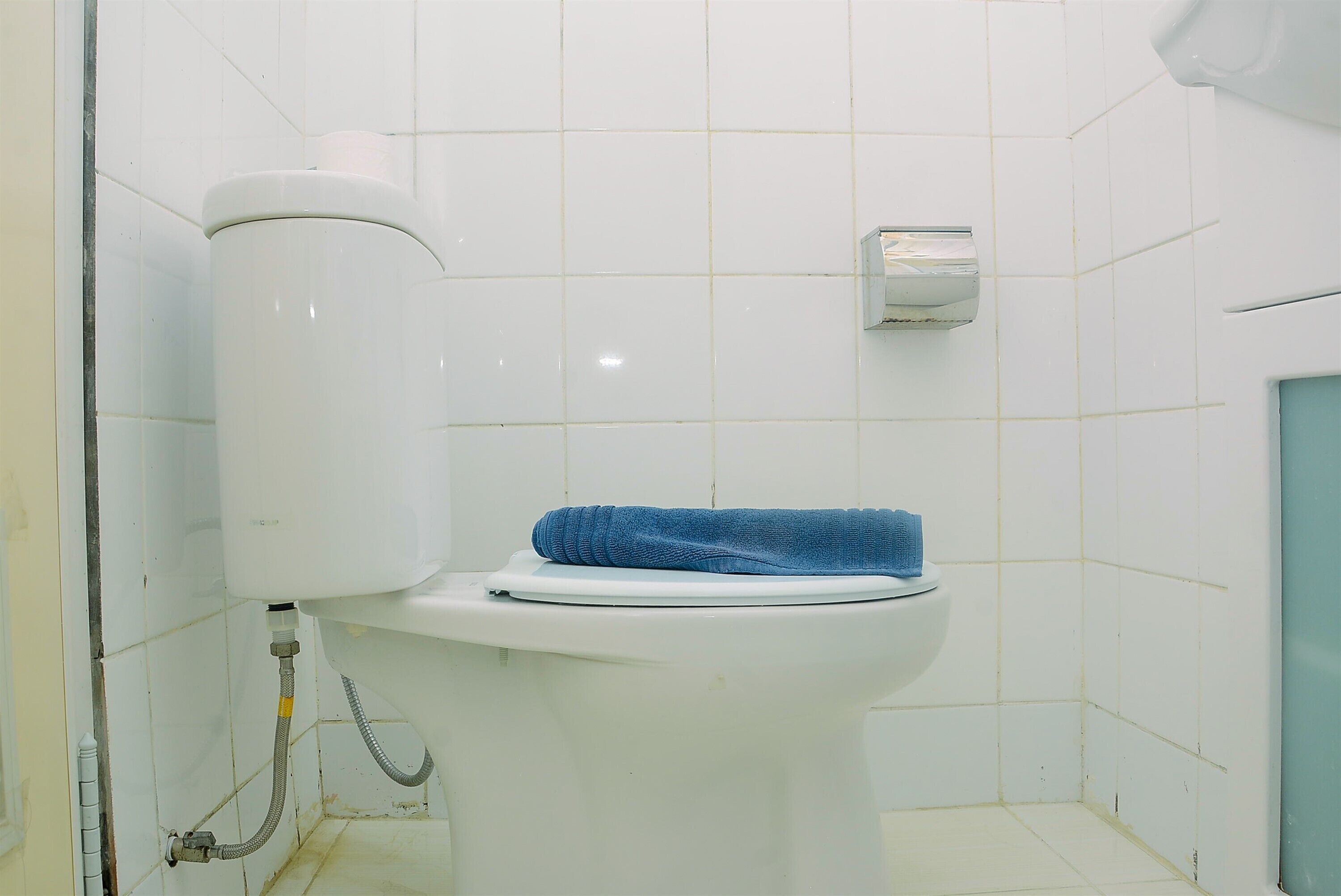 Valkoinen wc-istuin, jonka päällä on sininen pyyhe, valkoinen vesisäiliö ja seinään kiinnitetty bidee.