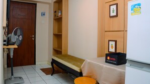 A small room with a wooden door, a single bed, a bedside table with a tray table, a standing fan, and a small stool. - Cozy Living with Modern Design 1BR Kebagusan City Apartment (Jakarta)