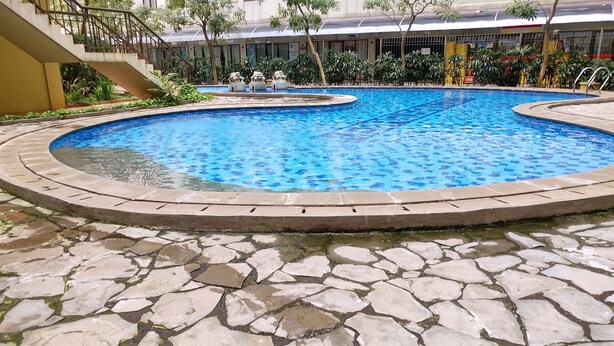 A circular pool with a stone border, surrounded by greenery and a staircase. - Cozy Living with Modern Design 1BR Kebagusan City Apartment (Jakarta)