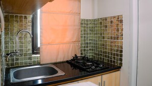 A compact kitchen with a gas stove, sink, and patterned tiles. - Cozy Living with Modern Design 1BR Kebagusan City Apartment (Jakarta)