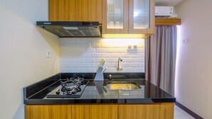 A kitchen with wooden cabinets, a black countertop, a gas stove, a stainless steel sink, and a built-in oven. - Comfortable 2BR Apartment at Cinere Resort (Depok)