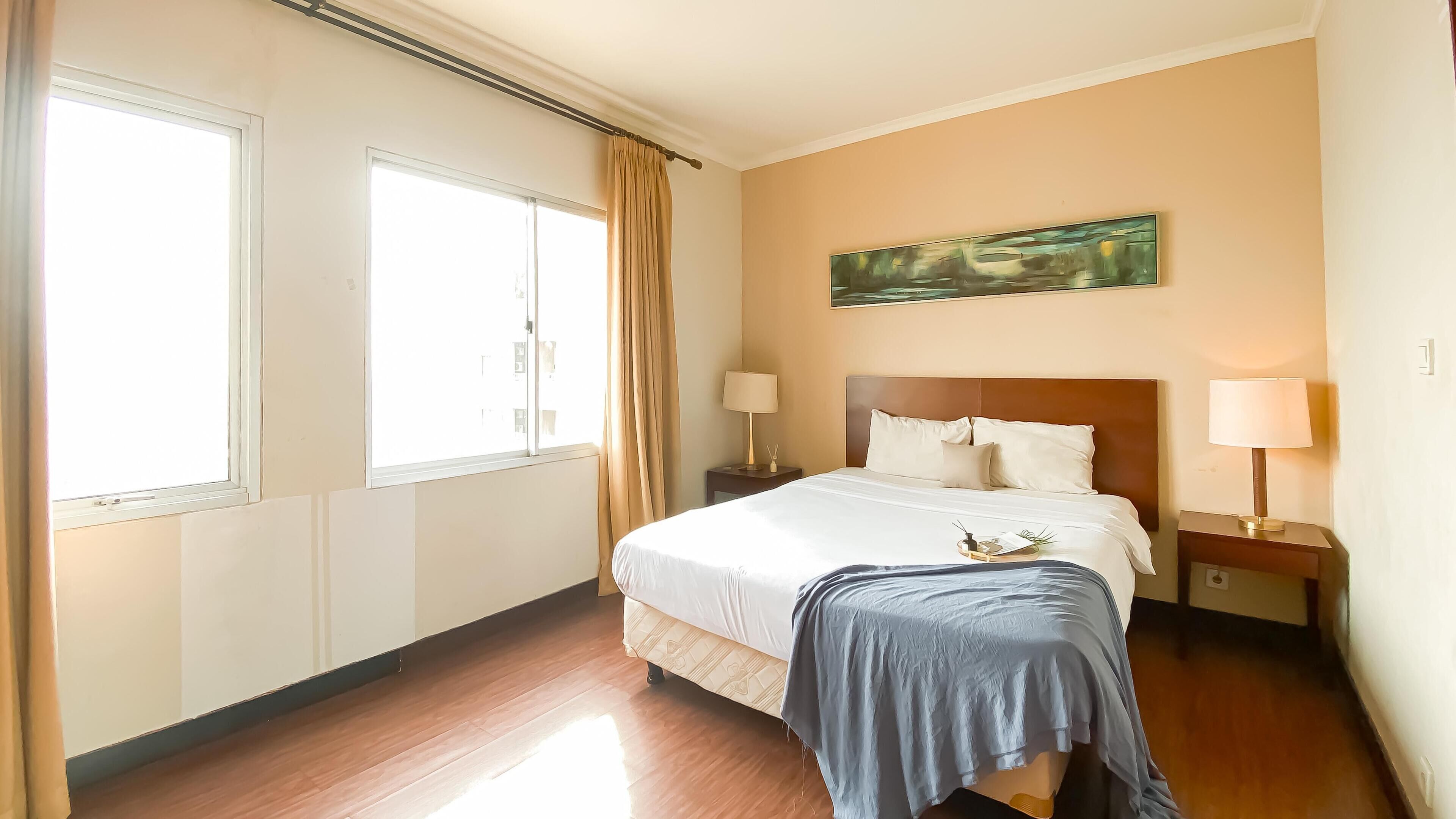 Habitación de hotel con una cama grande, dos mesitas de noche con lámparas, un cuadro en la pared y una ventana con cortinas.