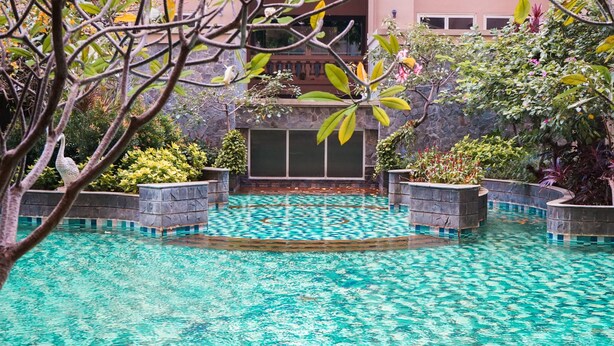 A swimming pool with clear water, surrounded by stone walls and potted plants. - 1BR Queen Bed at Ancol Marina Apartment near Dufan (Jakarta)