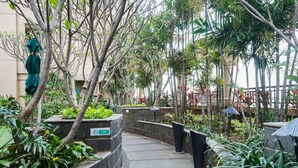 A courtyard with stone planters, a sign indicating a smoking area, and a variety of tropical plants. - 1BR Queen Bed at Ancol Marina Apartment near Dufan (Jakarta)