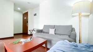 A modern living room with a grey sofa, a wooden coffee table with a magazine, a blue blanket, and a floor lamp. - 1BR Queen Bed at Ancol Marina Apartment near Dufan (Jakarta)