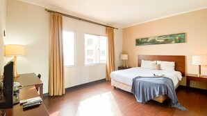 A hotel room with a bed, two bedside tables with lamps, a painting on the wall, and a window with curtains. - 1BR Queen Bed at Ancol Marina Apartment near Dufan (Jakarta)